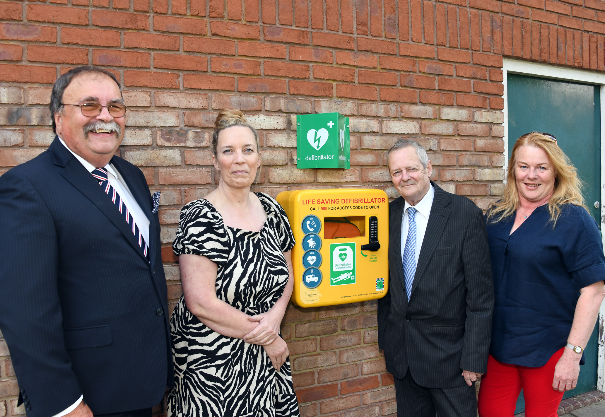 4 people in front of wall mounted defibrilator