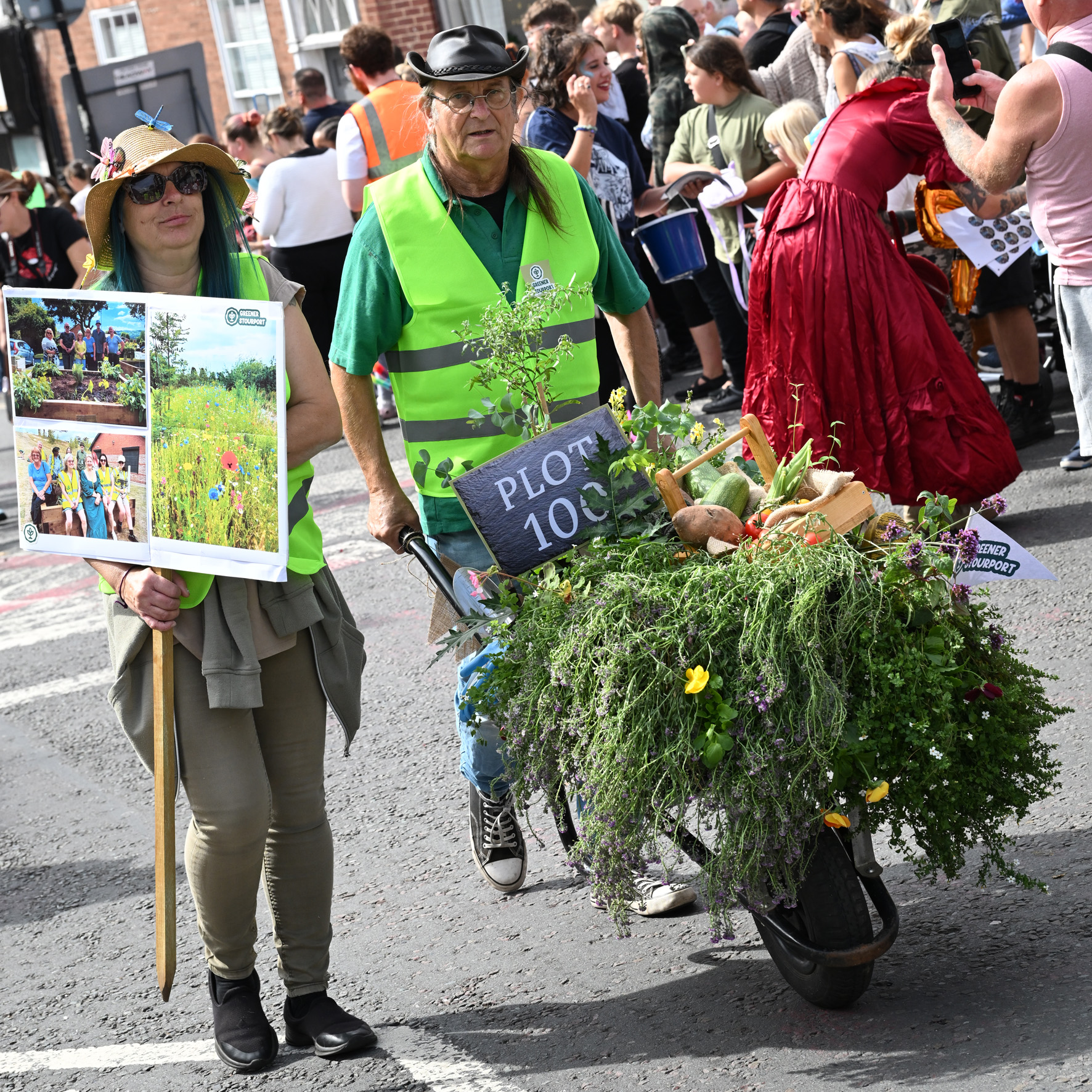 wheelbarrow full of produce being pushed by man in high vis vest as part of parade